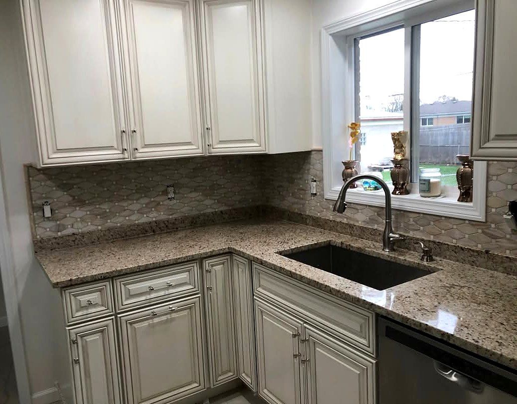 Arabesque mosaic tile kitchen backsplash with granite countertop and cream cabinetry
