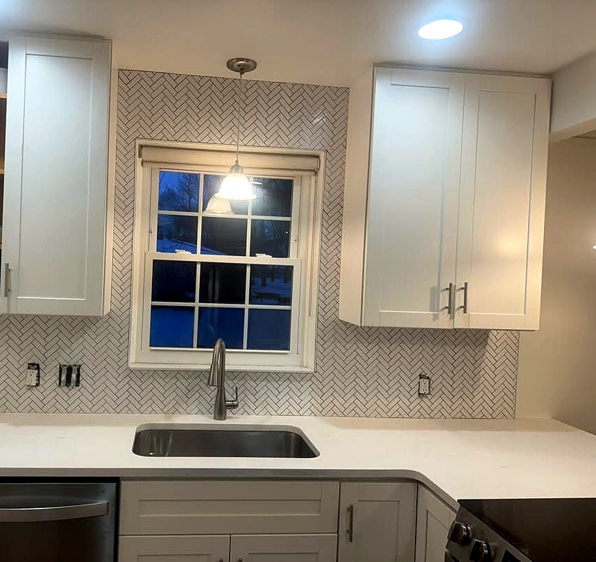 White herringbone tile kitchen backsplash installed around a window with dark grout