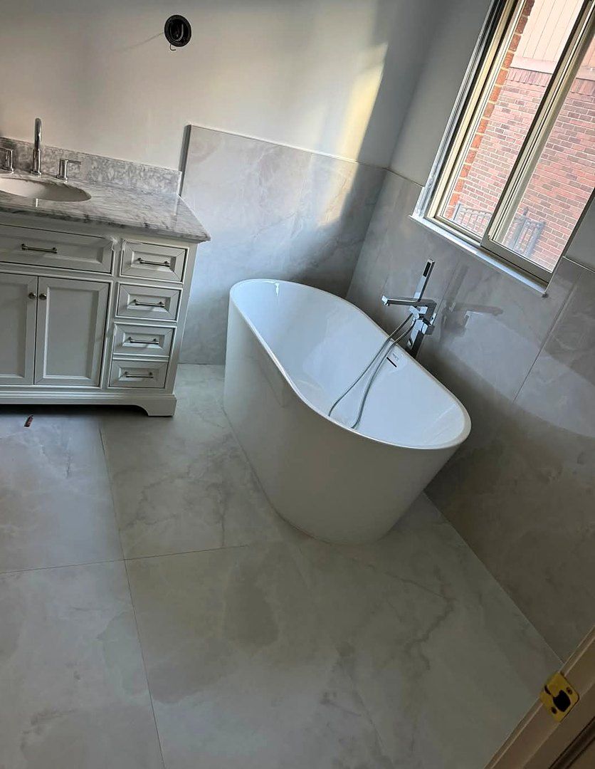 Master bathroom with large-format marble-look porcelain floor and wall tile around a freestanding tub
