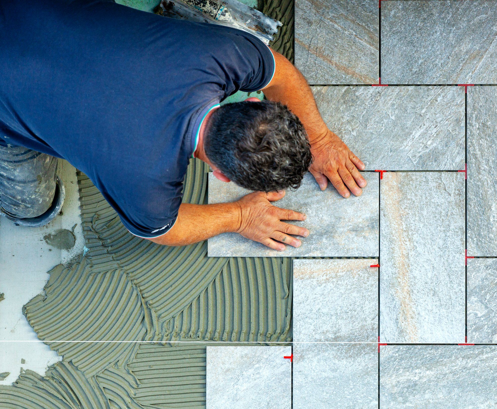 Large-format tile being set into combed thinset with levelling clips in the joints